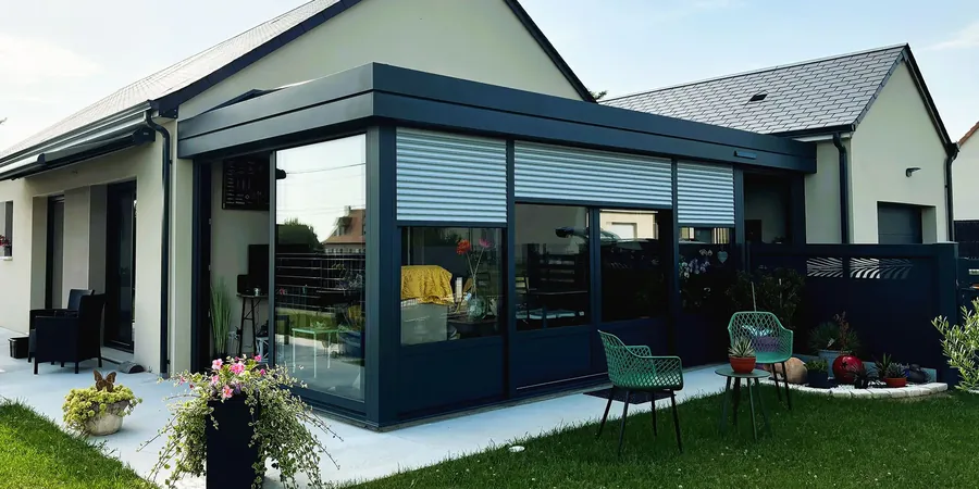 Véranda contemporaine sombre avec grandes baies et volets roulants, ouverte sur le jardin