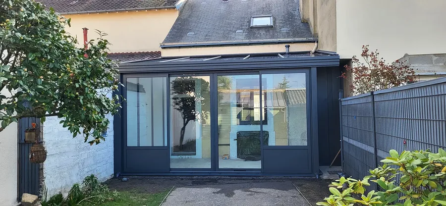 Véranda rénovée avec menuiseries sombres et portes vitrées donnant sur le jardin