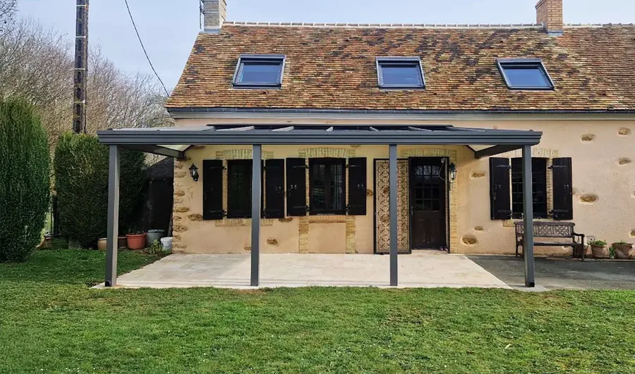 Pergola à toit fixe adossée à une maison en pierre