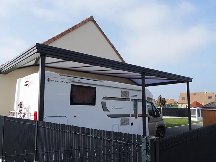 Camping-car stationné sous un carport haut adossé à une maison